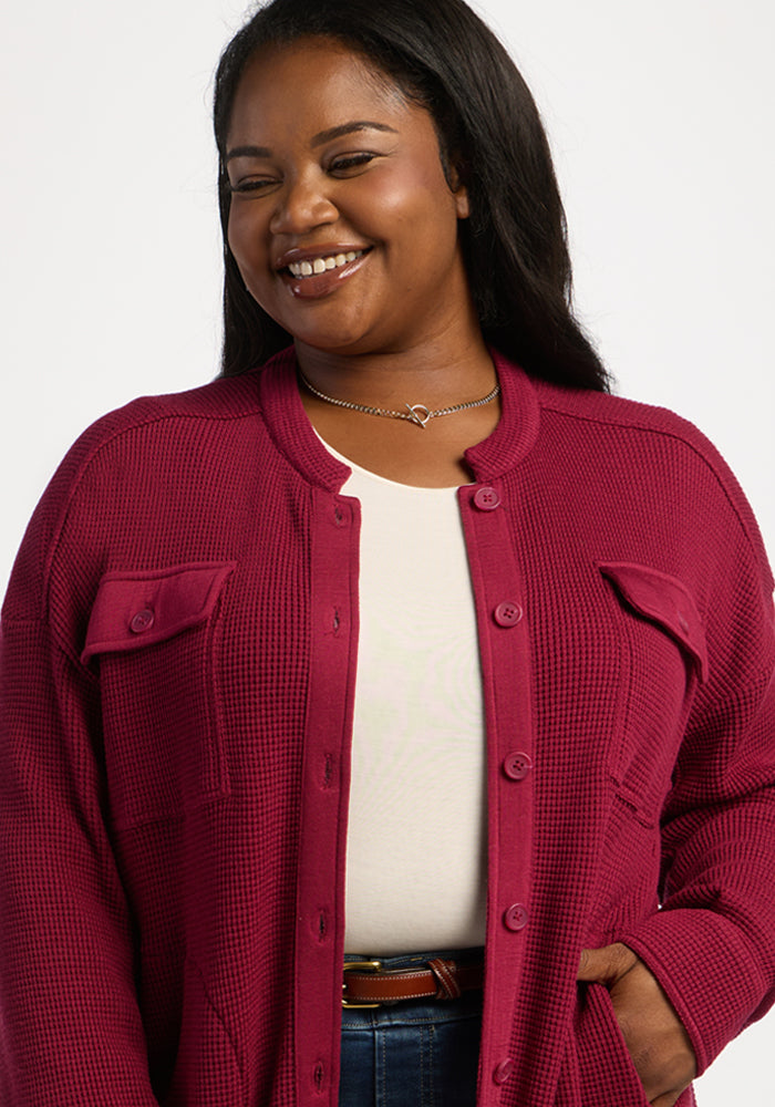 Woman smiling in a Woolx Oaklynn Waffle Shacket in Beet Red over a white top, one hand in pocket, plain background.