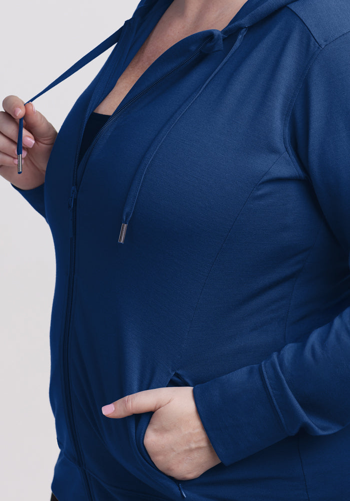 A person wearing the Woolx Ryann Hoodie in Estate Blue holds one drawstring with their left hand and has their right hand in the pocket, with only the torso and part of the lower face visible.