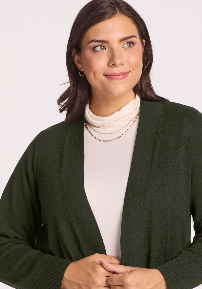 Woman in Woolx Macie Sweater - Duffel Bag, smiling in a cozy, dark green cardigan over a white turtleneck.