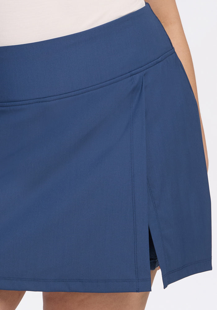 A close-up of a person wearing the Woolx Topanga Skort in Vintage Indigo, featuring a side slit and waistband detail. Paired with a white top, it highlights this stylish moisture-wicking activewear piece.