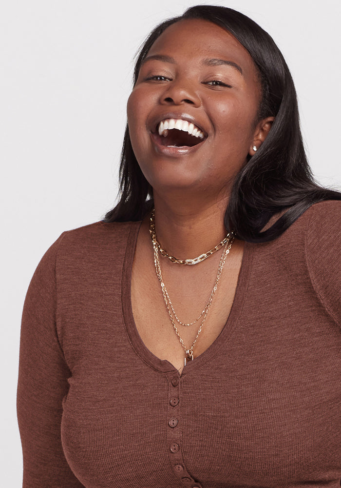 Woman with long dark hair in Woolx Reese Ribbed Henley - Sable Heather, wearing gold necklaces and smiling.