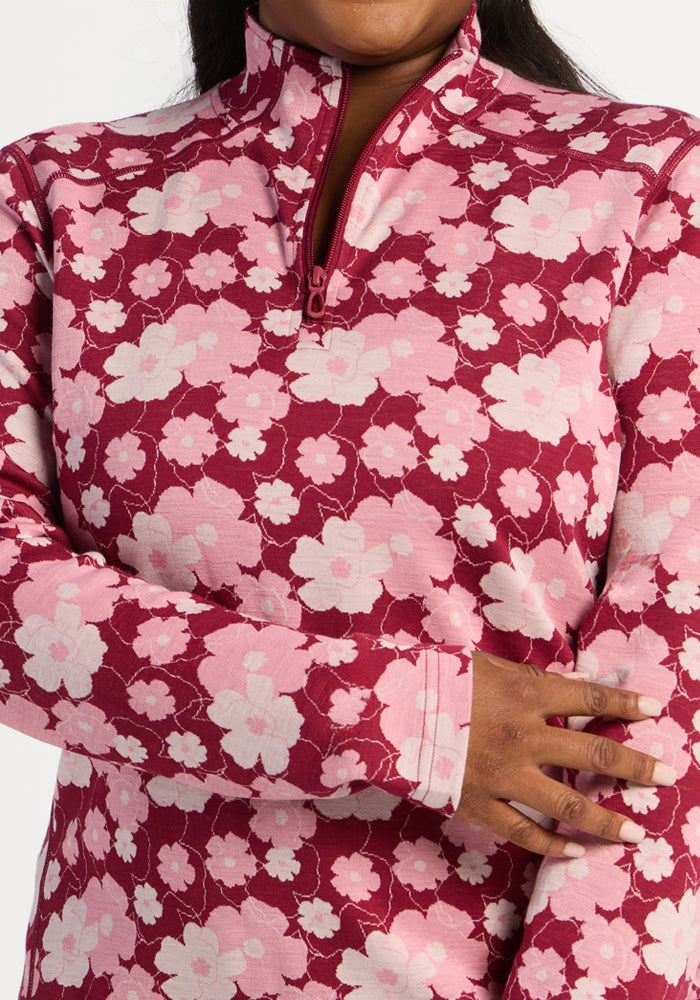 Someone wears the Woolx Emi 1/4 Zip - Floral Crush, a pink and red floral Merino wool top, with one arm crossed.