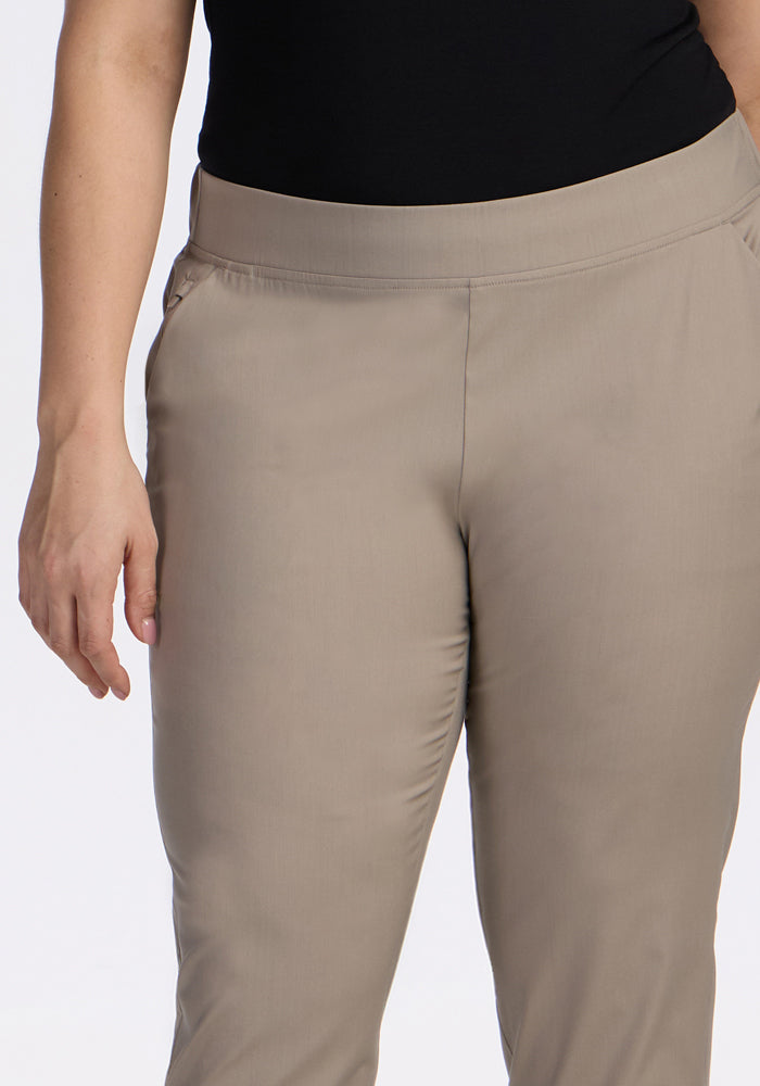 A person is shown from mid-torso to mid-thigh against a plain background, wearing the Woolx Nicole Tall Ankle Pant in Vintage Khaki with a black top, one arm relaxed at their side.