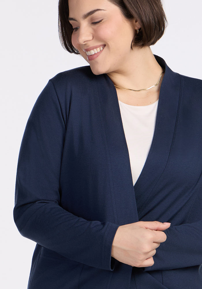 A woman with short brown hair smiles and looks down, wearing the Woolx Paisley Cardigan in Deep Navy over a white top and a thin gold necklace.