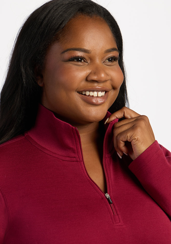 Smiling woman in Woolx Brooke 1/4 Zip - Beet Red, holding collar and looking to side on white background.