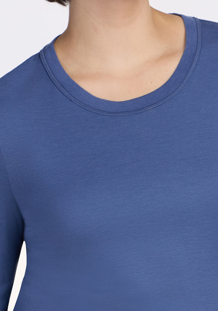 A person wears the Woolx Hazel Tunic - Skyline, a long-sleeved, blue crewneck made from moisture-wicking, temperature-regulating fabric. Only the neck, shoulders, and upper chest are shown; the face is mostly out of view.