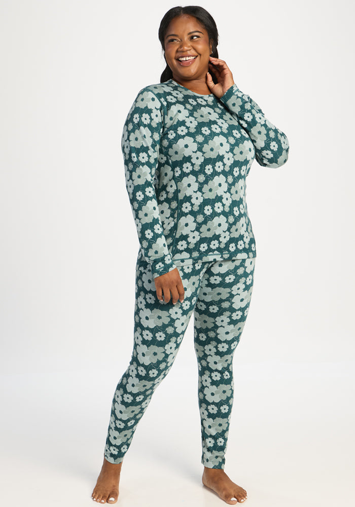 Smiling woman in Woolx Maddie Baselayer Top - Coastal Wildflower stands barefoot, touching her neck.
