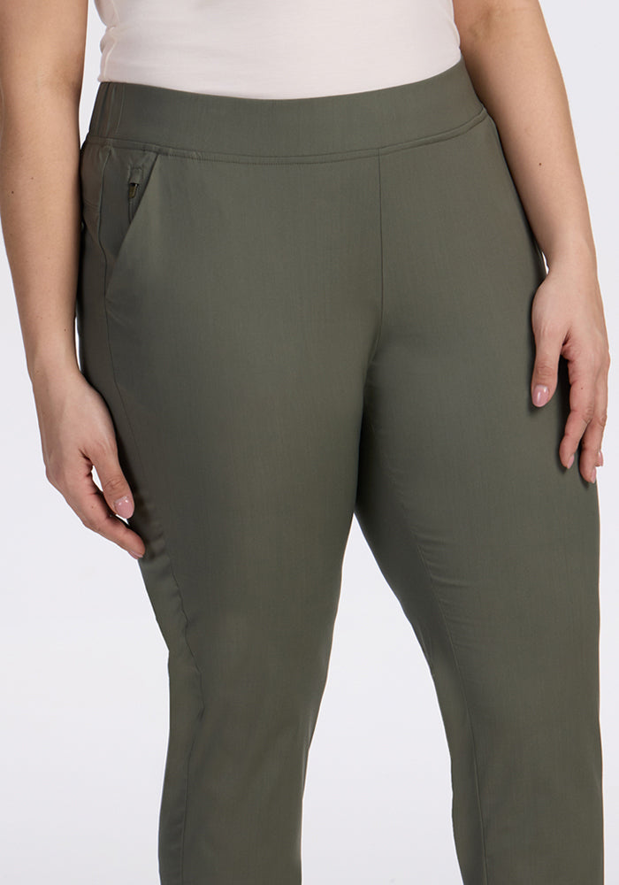 A person models the Woolx Nicole Ankle Pants in Sage Olive, paired with a white top. The photo shows them from mid-torso to mid-thigh, one hand by their side and the other partially tucked into a pocket.