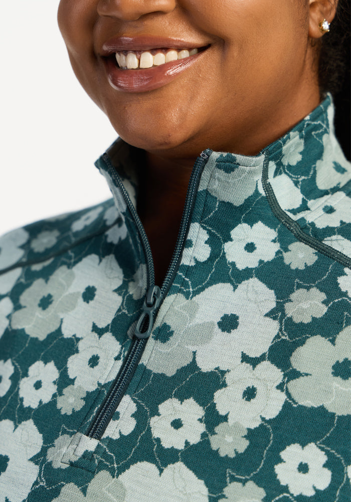 A person smiles, wearing Woolx Emi 1/4 Zip - Coastal Wildflower with moisture-wicking fabric and the zipper partly open.