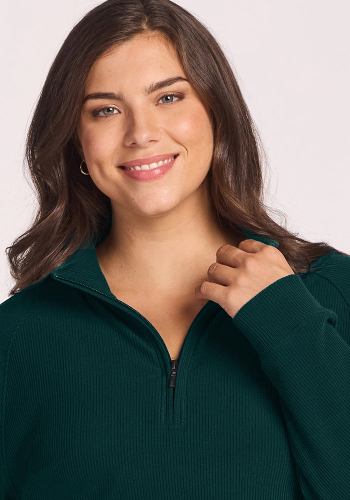 Woman with long brown hair in a Woolx Quinn Ribbed 1/4 Zip - Deep Pine, smiling at the camera against a light background.