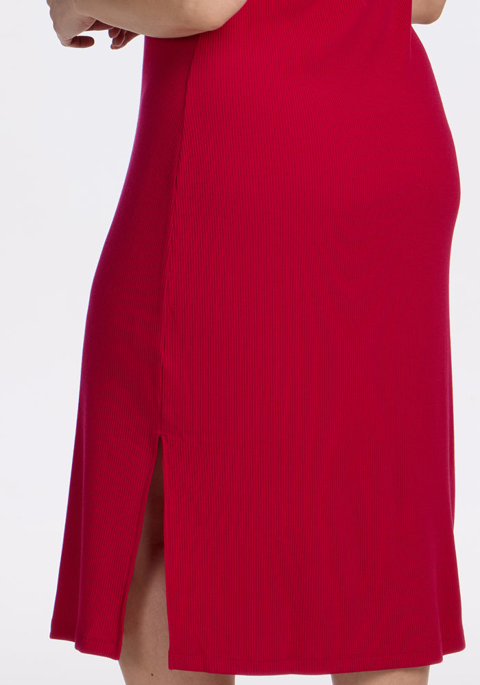 A close-up of a person wearing the Woolx Iris Ribbed Dress in Poppy Spark, featuring merino wool fabric and a side slit, with part of their arm and leg visible against a plain white background.