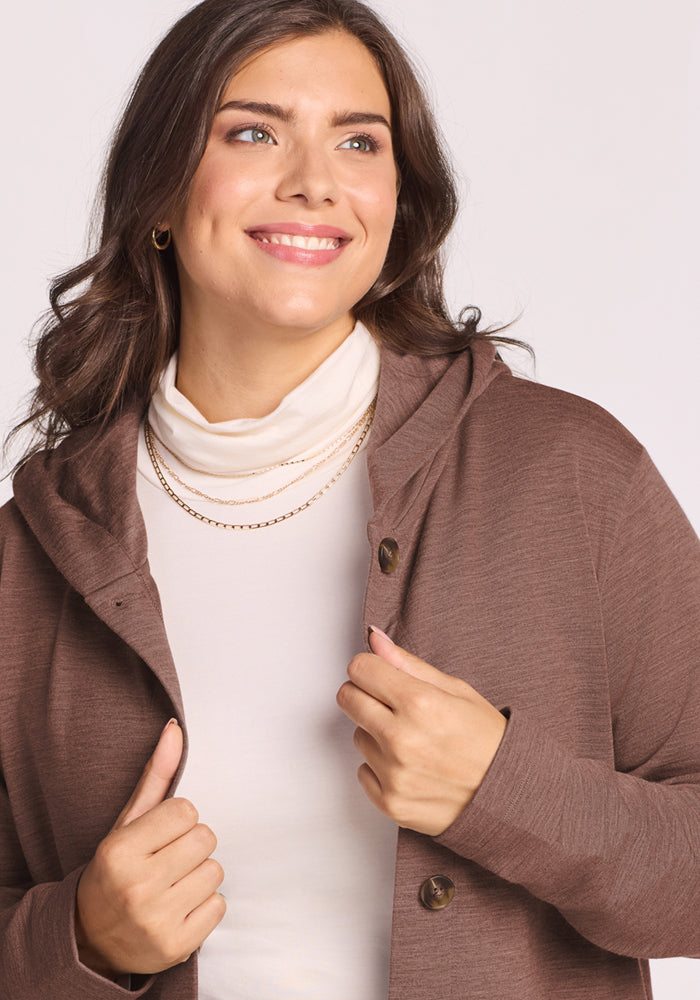 Smiling woman in Woolx Edna Hooded Cardigan in Sable Heather over a cream turtleneck, holding the collar.