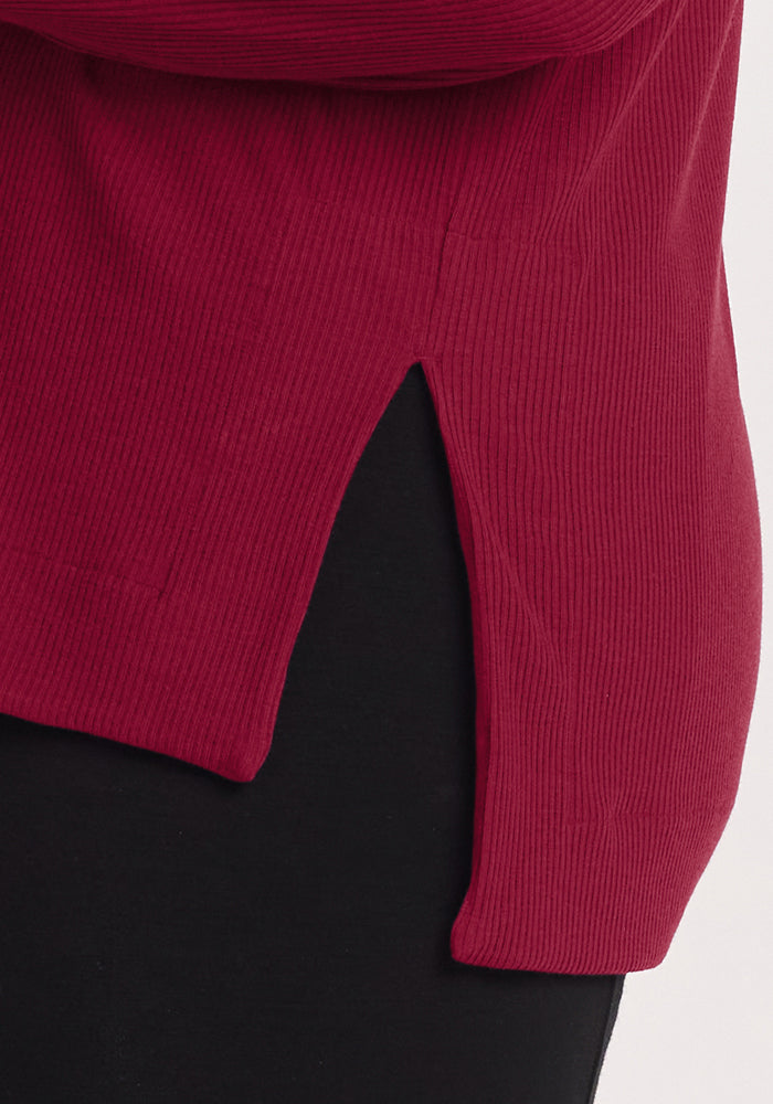 Close-up of the Woolx Ainsley Sweater in Beet Red with a side slit, styled with black pants for a chic look.