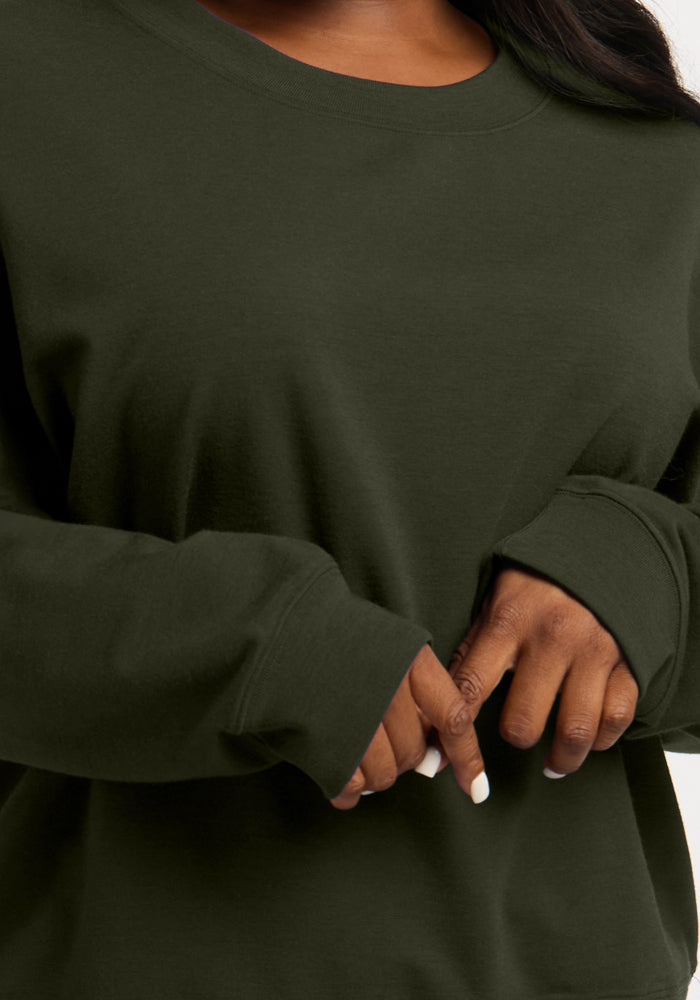 A person wearing a dark olive green, temperature-regulating merino wool Molly Crewneck - Duffel Bag long-sleeve shirt.