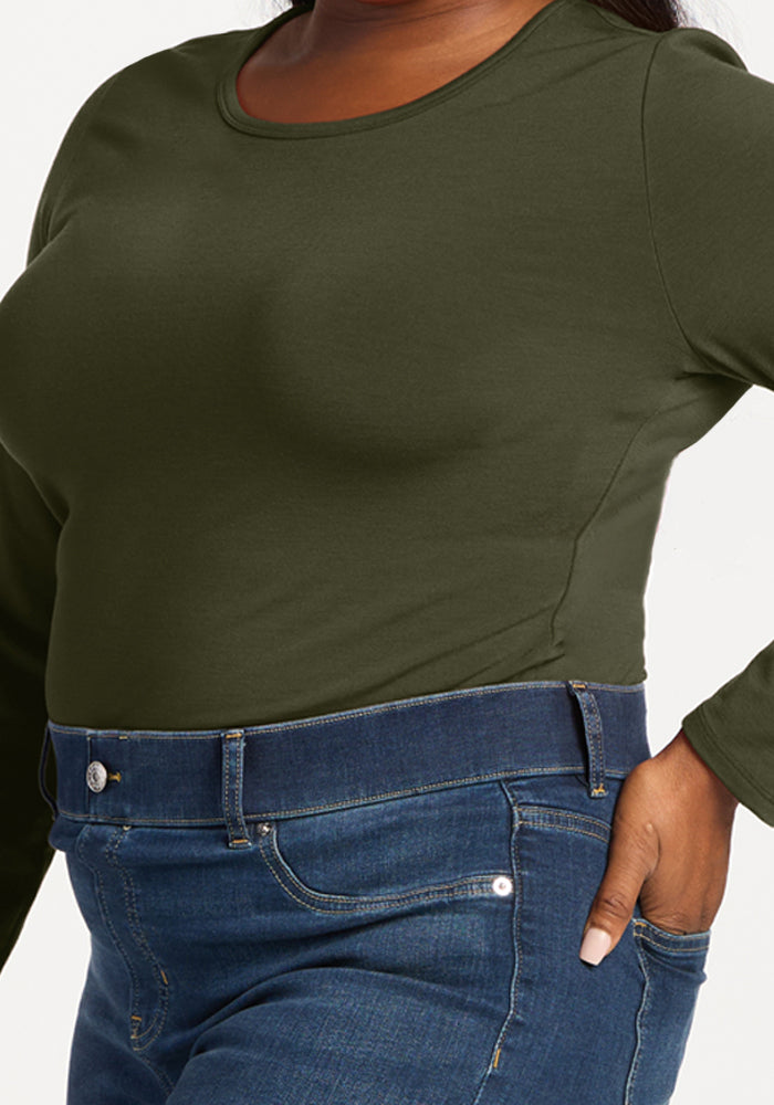 Woman in Woolx Margot Bodysuit - Everleaf, olive green, long sleeves, blue jeans, hand on hip, white background.