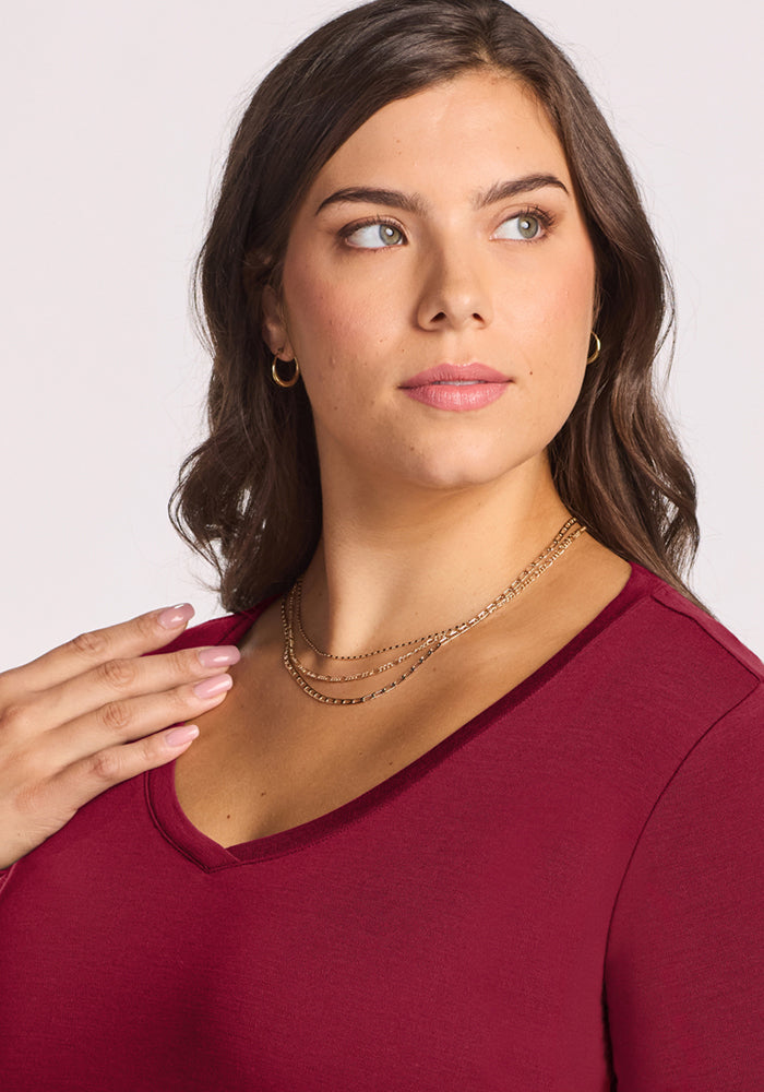 Woman in the Woolx Eva Tunic - Beet Red, styled with gold necklaces and hoops—a winter wardrobe staple.