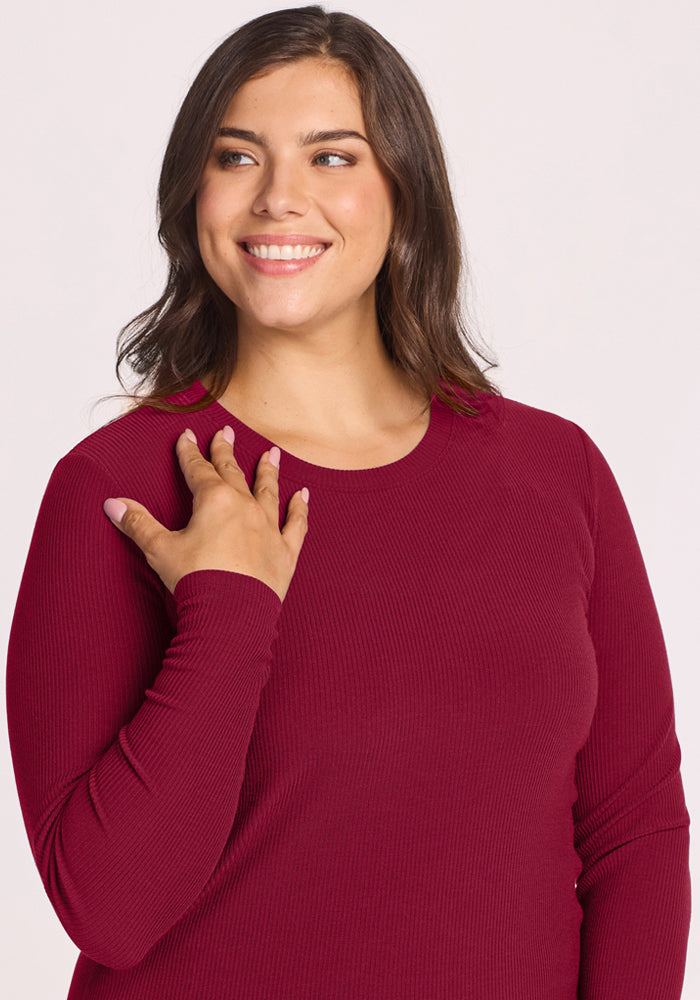 Smiling woman in a Woolx Hadley Ribbed Crew - Beet Red touches her shoulder, gazing off to the side.