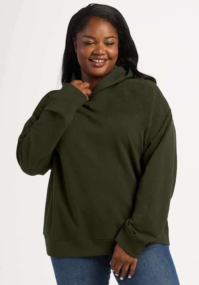 A woman wearing a dark olive green Genevieve Hoodie - Duffel Bag and blue jeans.