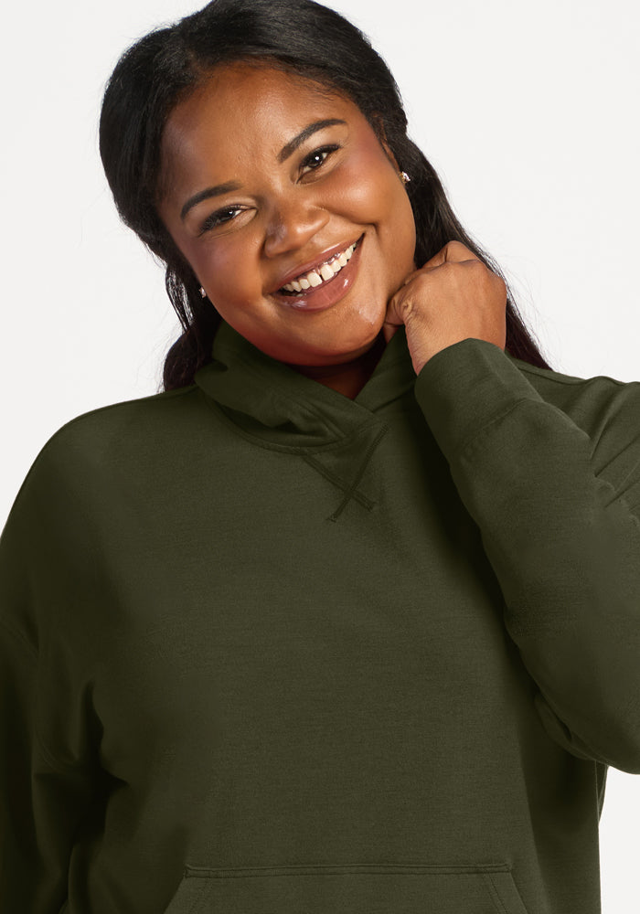 Smiling woman in a Woolx Lizzy Hoodie - Everleaf, hand at chin, posed before a plain white background.