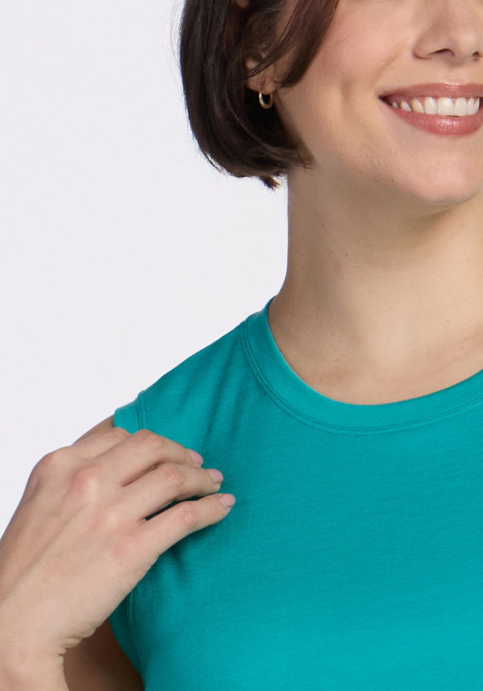 A person with short brown hair wears the Woolx Bella Tunic Top in Cool Jade, smiling as they touch their shoulder. Only the lower half of their face and upper torso are visible.