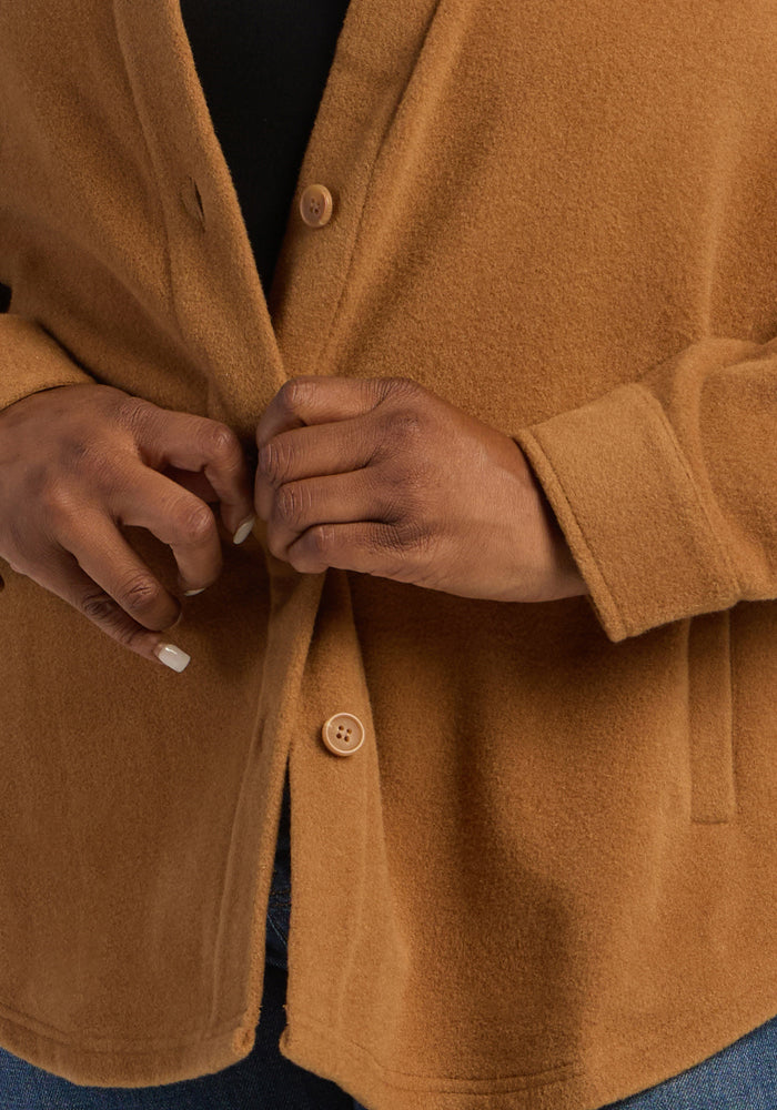 Hands button the Woolx Jovie Shacket - Saddleback, layered over a dark top and jeans; focus on torso only.
