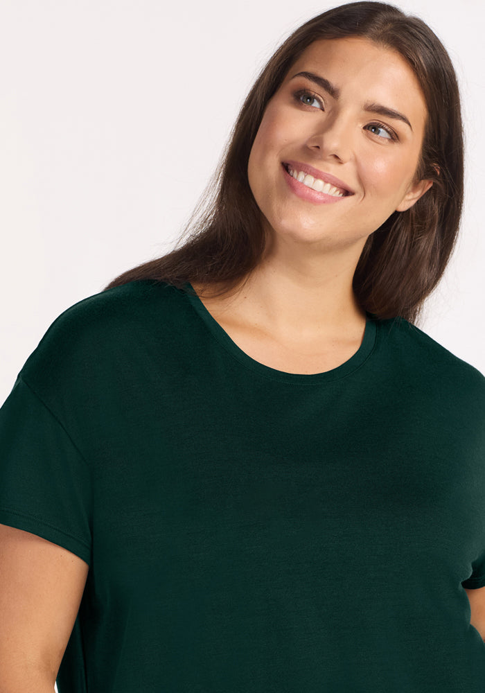 A smiling woman wearing a dark green Billie Lounge Tee - Deep Pine moisture-wicking Merino wool pajama top.