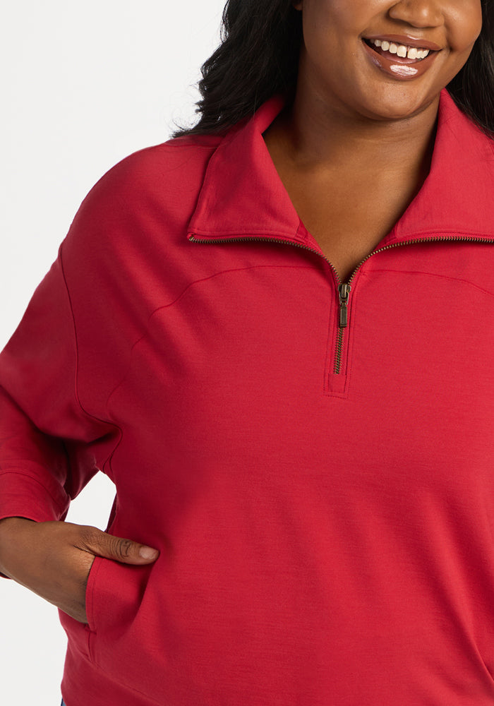 A smiling person wearing a red Woolx Tori 1/4 Zip - Maraschino Cherry merino wool quarter zip pullover with pockets.
