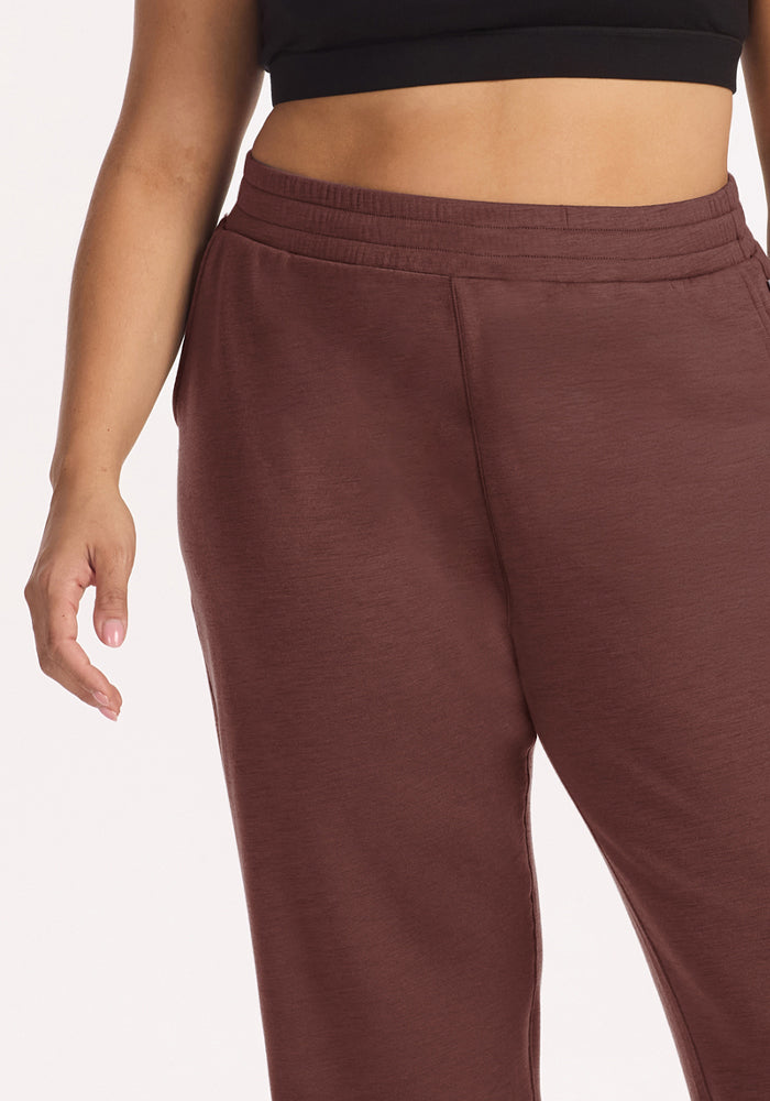 Someone wears Woolx Parker Sweatpants in Canyon Clay and a black crop top, their left arm relaxed at their side.