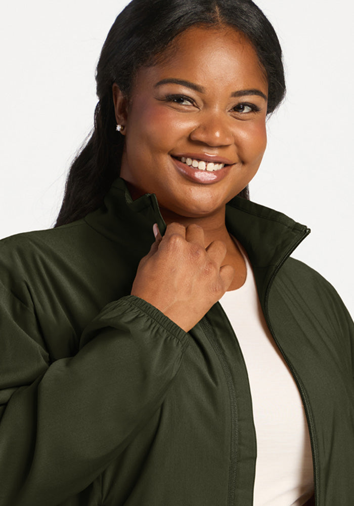 A smiling person wearing a forest green, all-season woven Cooper Windbreaker - Duffel Bag with a customizable fit.