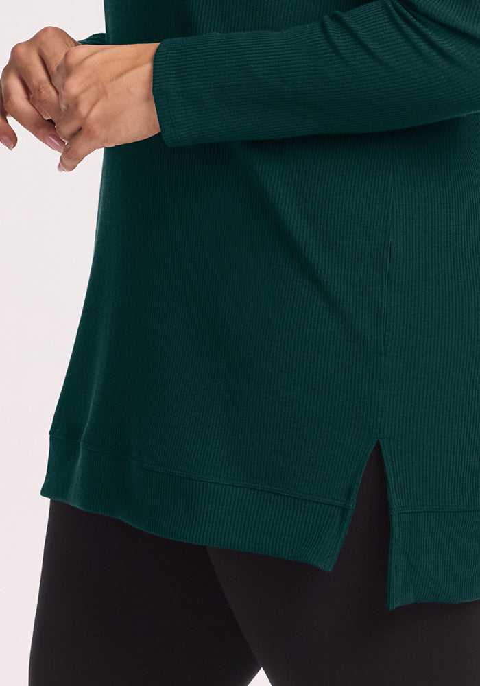 Person wearing Woolx Evie Ribbed Tunic in Deep Pine and black leggings, hands near waist.