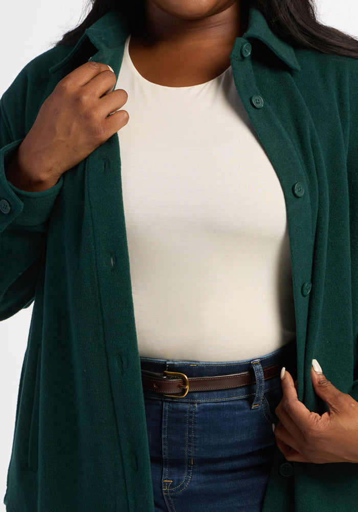 Woman styles her look with the Woolx Jovie Shacket in deep pine, layered over a white top and blue jeans.