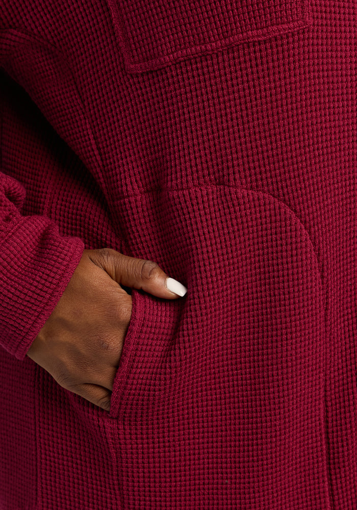 A hand with white nails is tucked into the pocket of the Woolx Oaklynn Waffle Shacket in Beet Red.
