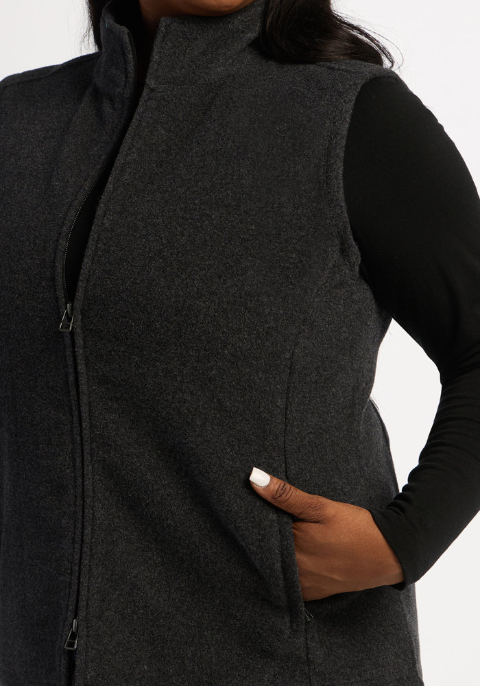 Model wears Woolx Haley Vest - Carbon Black over a black long-sleeve, hand tucked in the vest pocket.