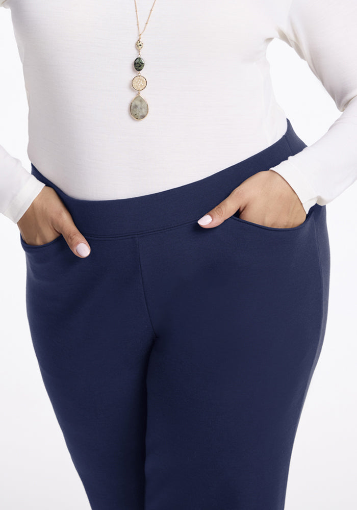 Person in a white top, Woolx Ellie Wide Leg Pants - Ocean Cavern, pendant necklace, hands in pant pockets.