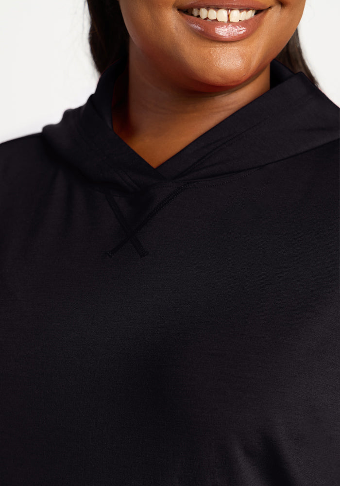 Woman smiling in the Woolx Lizzy Hoodie in black, buttery soft fabric, shown neck to chest on a white background.