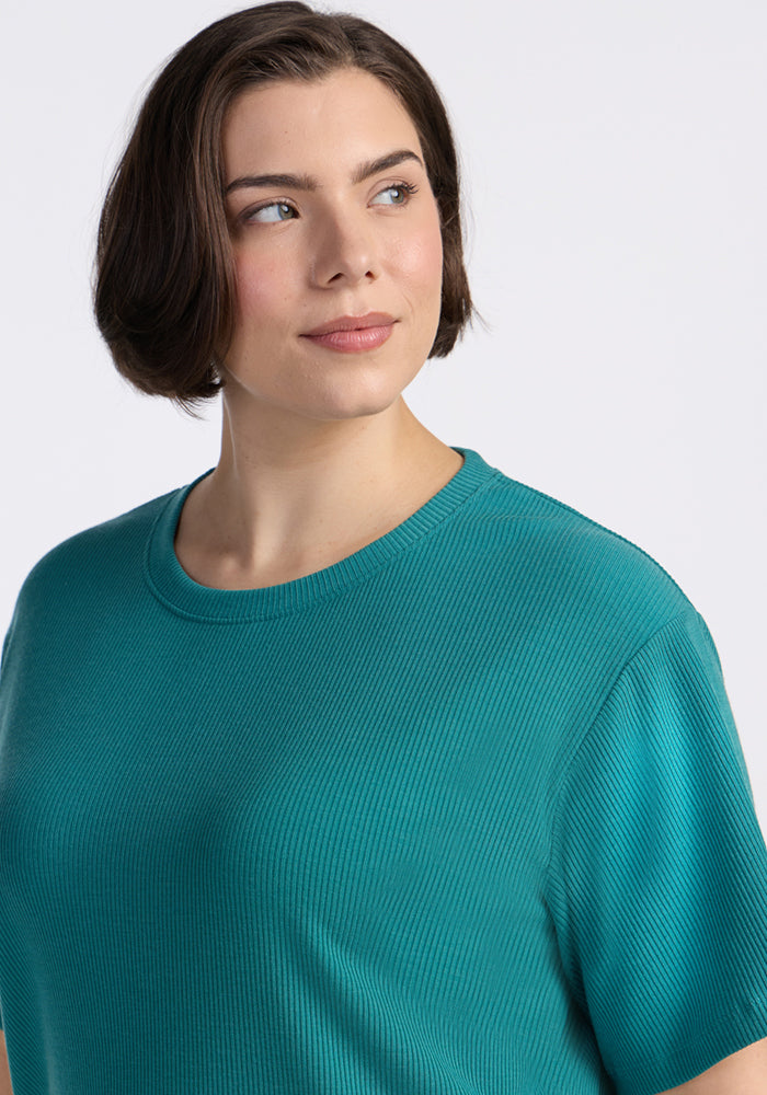 A person with short brown hair wears the Woolx Delia Ribbed Short Sleeve in Surfside, smiling slightly as they look to the side against a plain light background.