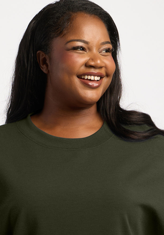 A smiling woman wears a forest green Molly Crewneck - Duffel Bag merino wool crewneck sweatshirt.