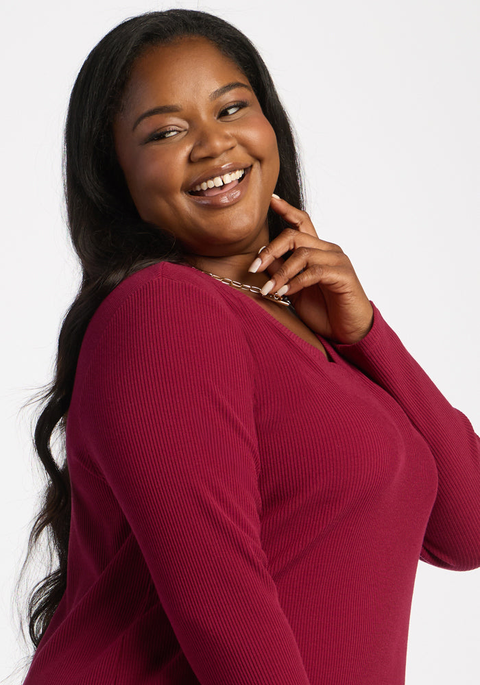 Smiling woman touches her face in a cozy Woolx Evie Ribbed Tunic—Beet Red—against a white background.