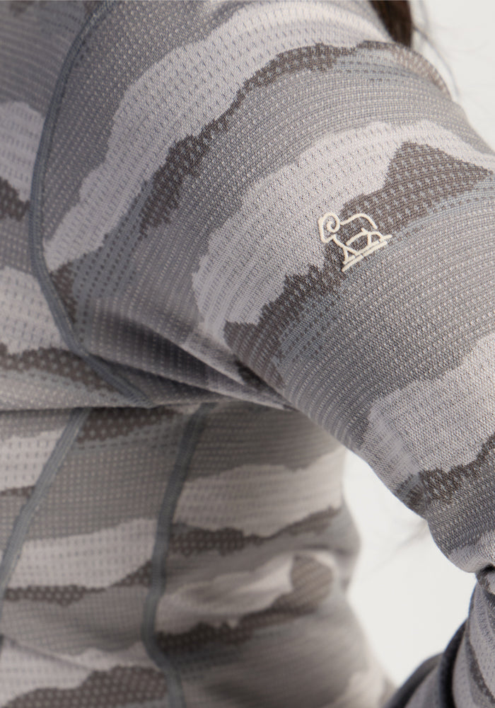 Close-up of Woolx Maddie Baselayer Top - High Peaks sleeve in gray camo with a small white elephant logo.