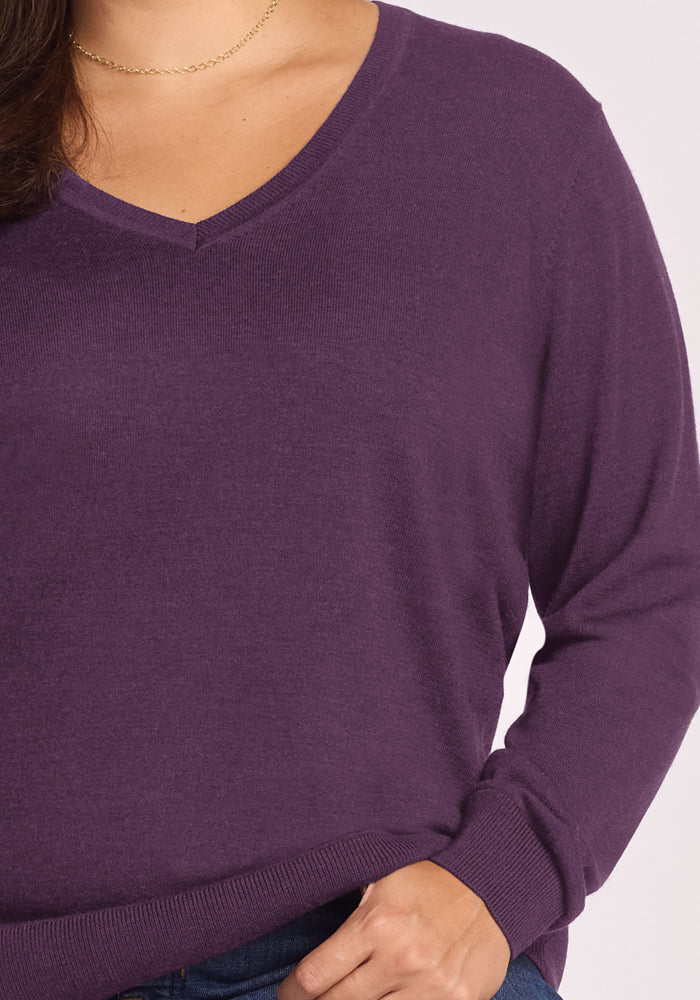 Someone wears the Woolx Francesca Sweater in Purple Iris with blue jeans, one hand casually in their pocket.