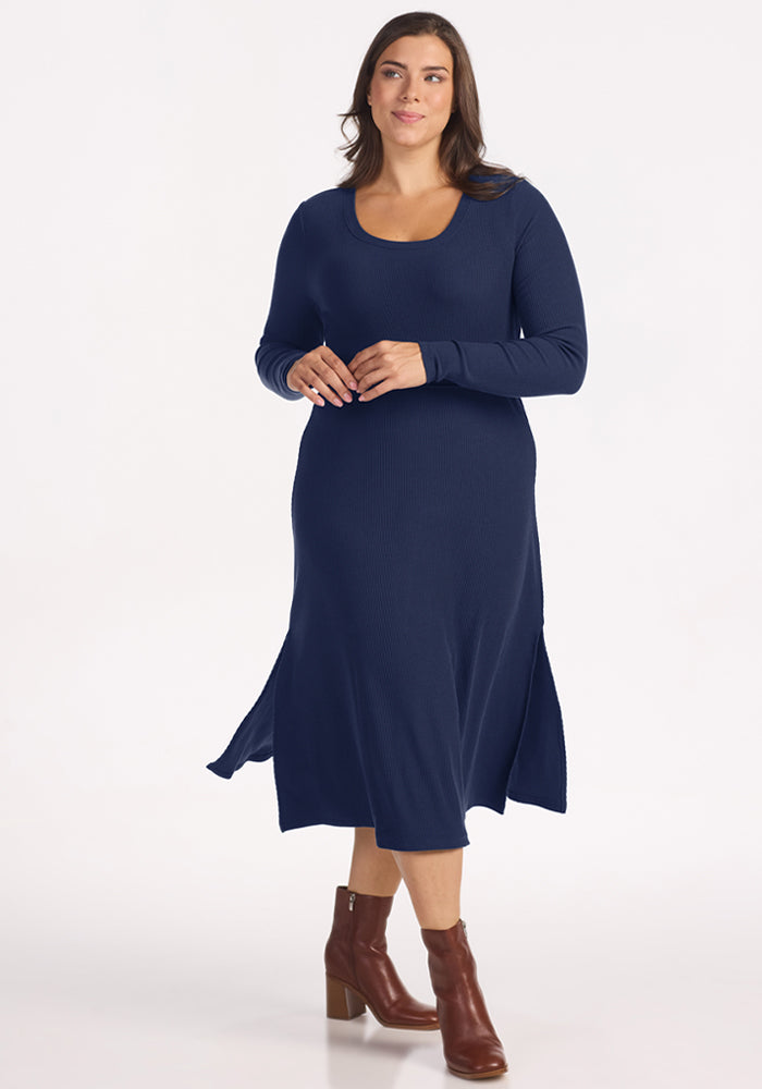 Woman wears Woolx Caroline Ribbed Twirl Dress - Ocean Cavern with brown ankle boots, against a white background.