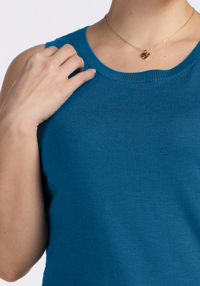 Person wears a Woolx Chessy Tank Top in Blue Pine and a gold heart necklace, one hand touching the neckline.