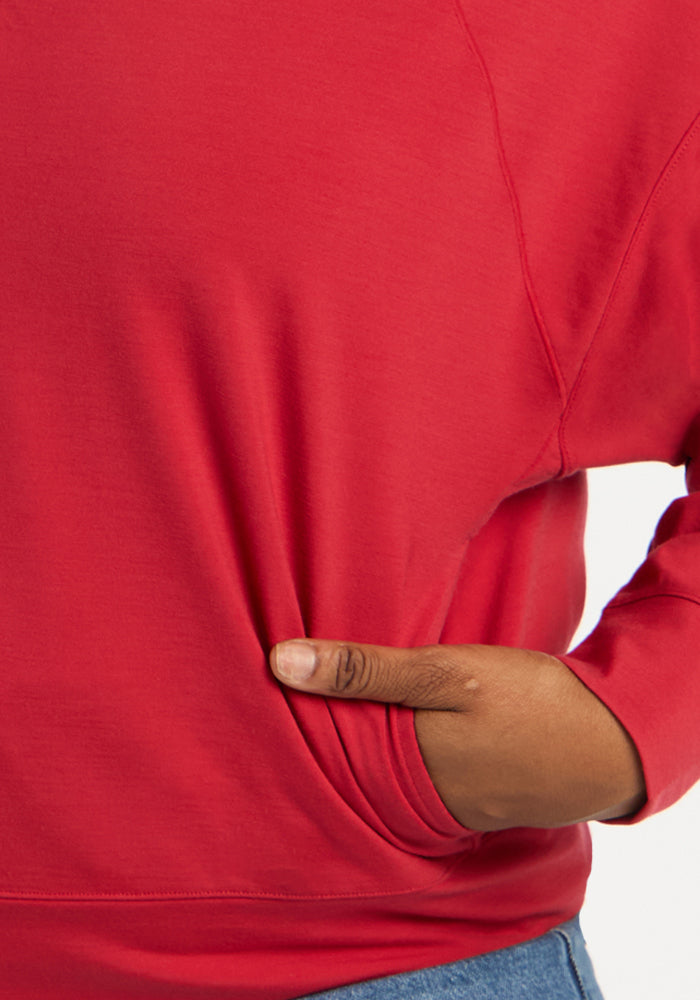 Hand tucked into the front pocket of a red Tori 1/4 Zip - Maraschino Cherry merino wool quarter zip.