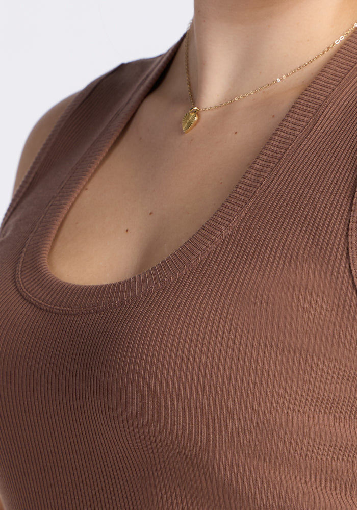 A close-up of a person wearing the Woolx Sloane Ribbed Tank in Sienna Kiss and a delicate gold necklace with a small heart-shaped pendant.
