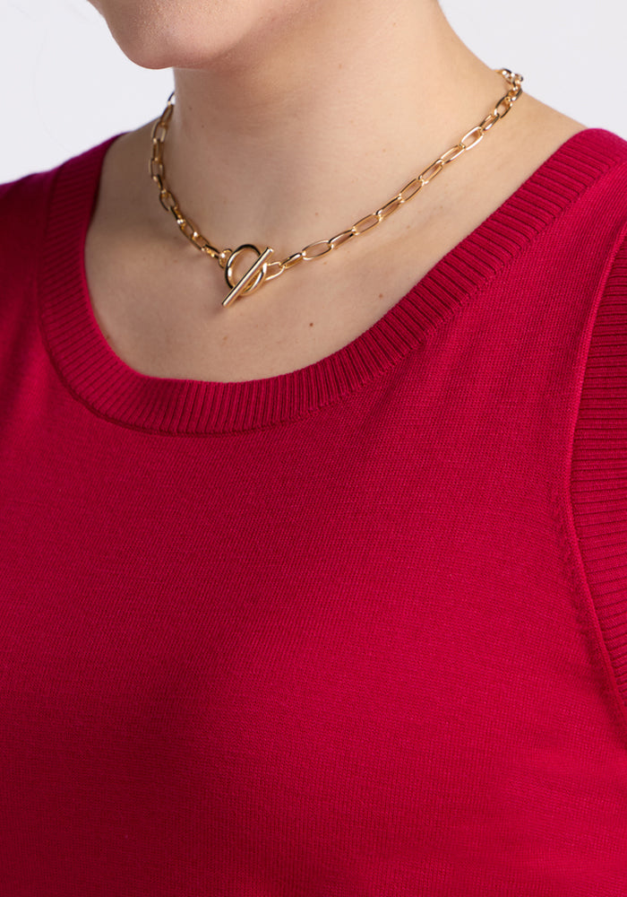 A person wearing a gold chain necklace with a toggle clasp and the Woolx Chessy Tank Top in Poppy Spark, a bright red ribbed merino wool piece perfect for layering. Only their lower face, neck, and upper chest are visible.