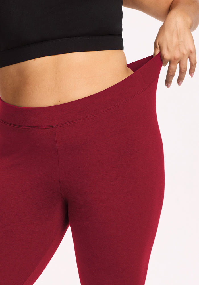 Model in Woolx Stella Leggings - Pinot Noir pulls waistband to reveal flattering fit; midsection and hand shown, no face.