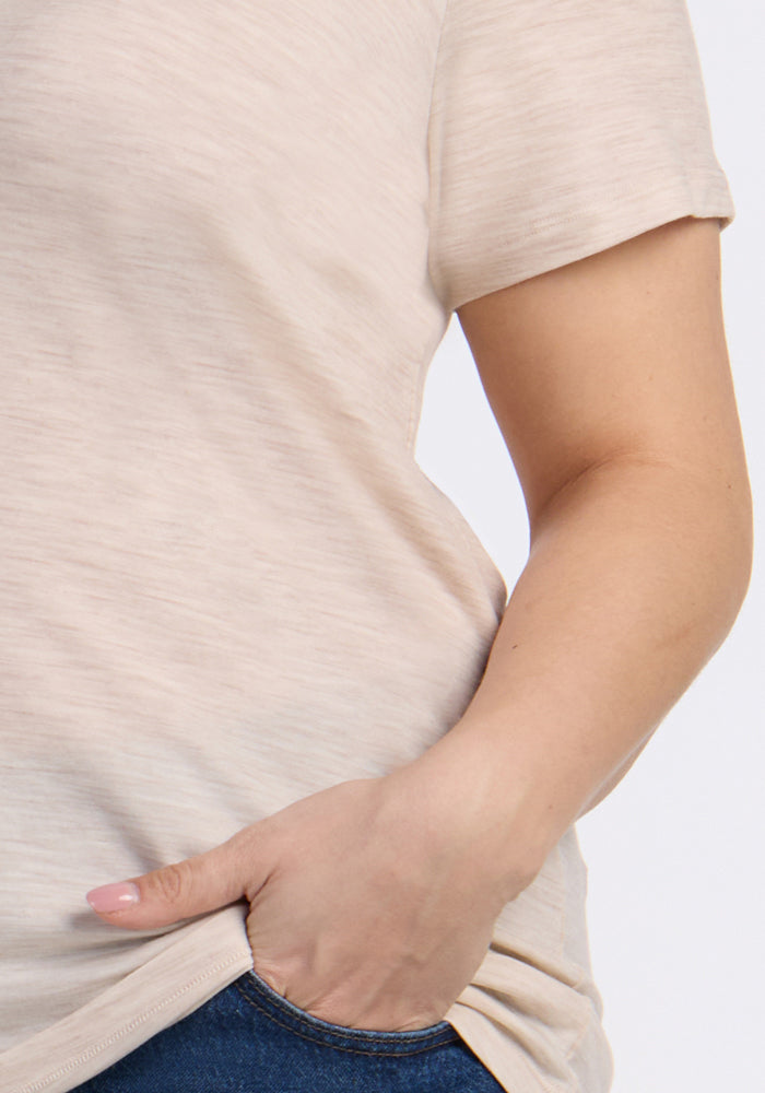 Close-up of a person wearing the Woolx Junie V Neck in Cream Heather, styled with blue jeans and their left hand in their pocket, set against a plain light background.