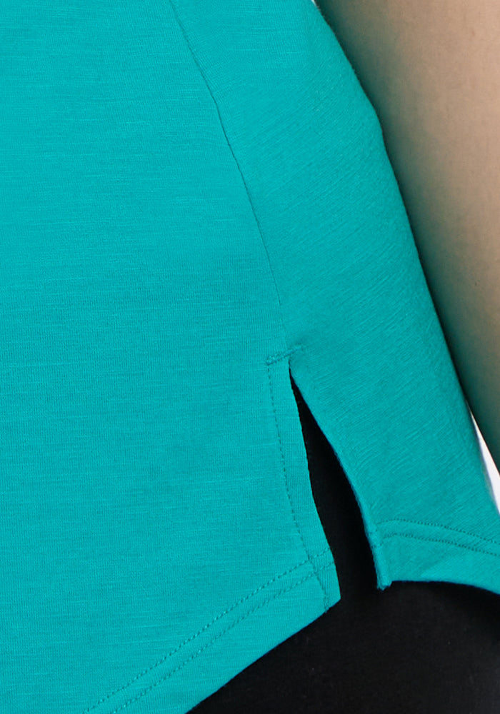 Close-up of the Woolx Bella Tunic Top in Cool Jade, a lightweight summer style with a side slit hem, showing part of a person's arm and black pants underneath.