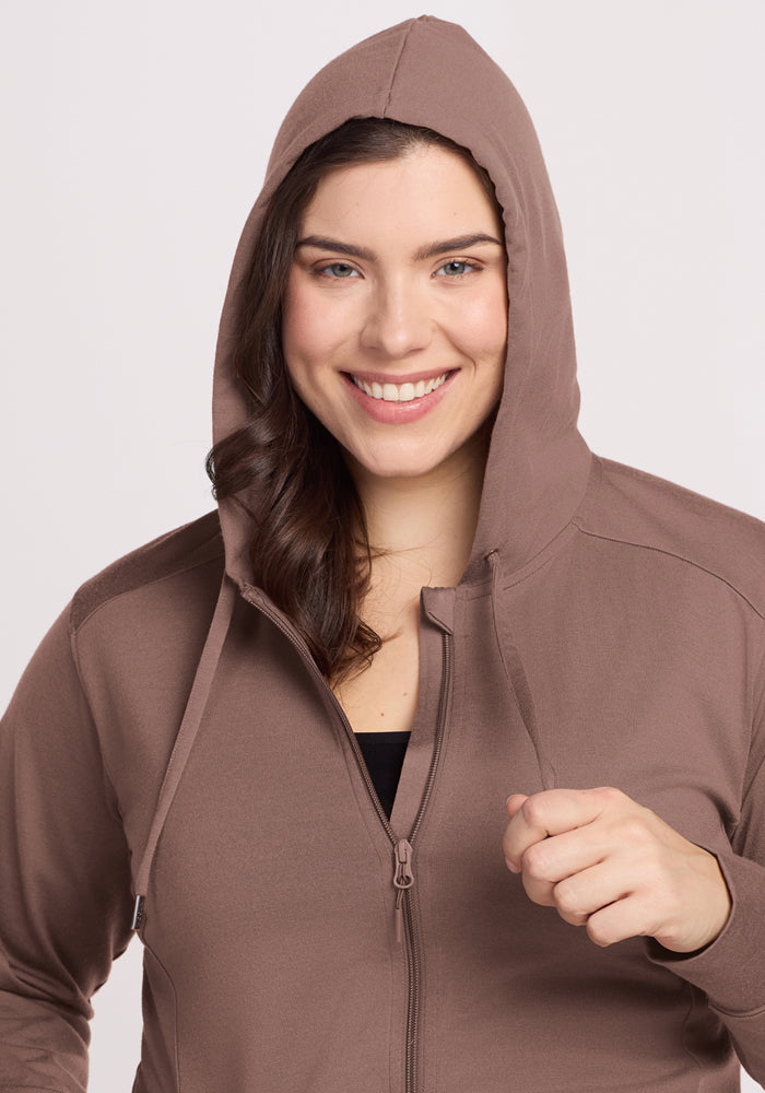Woman smiles in the Woolx Ryann Hoodie - Toasted Almond, a moisture-wicking merino essential with drawstring—travel ready.