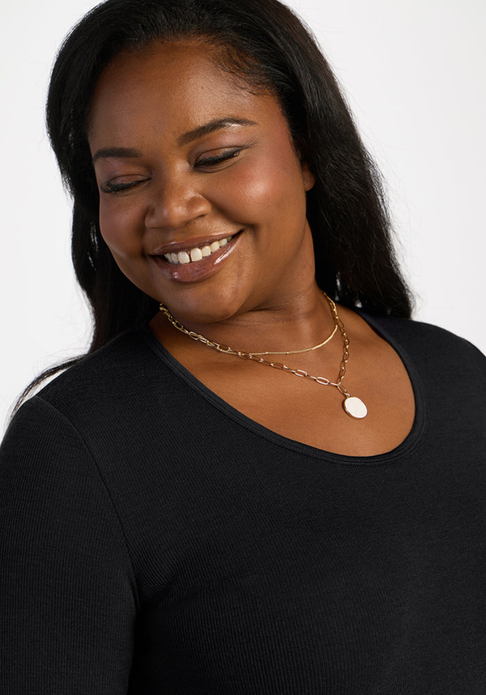 Smiling woman in Woolx Katie Ribbed Long Sleeve - Black, styled with gold necklaces, against a plain backdrop.